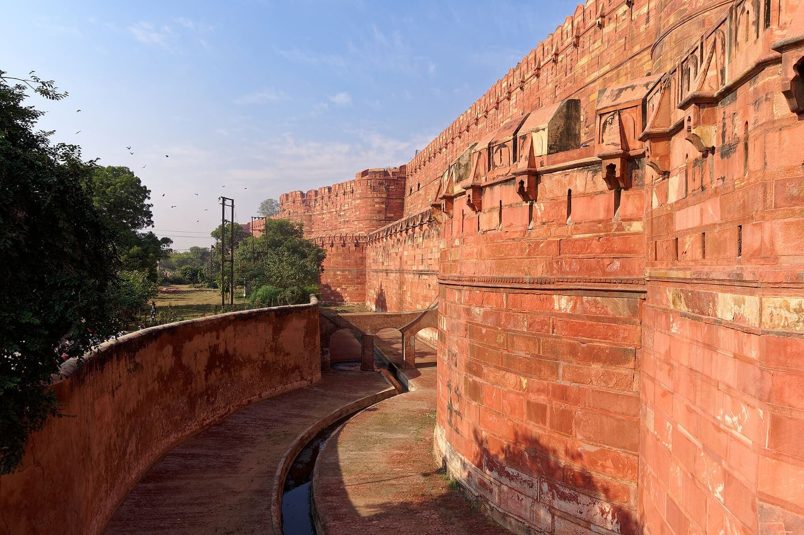 Agra Fort’s red sandstone ramparts rising above the dry moat in bright daylight
