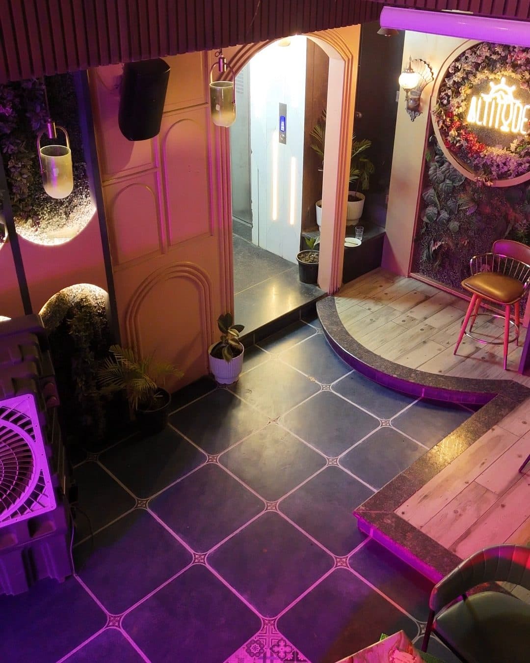 An arched doorway lit in soft pink beside a ring of flowers around the glowing ALTITUDE name, with a bar stool and a tiled floor in the foreground