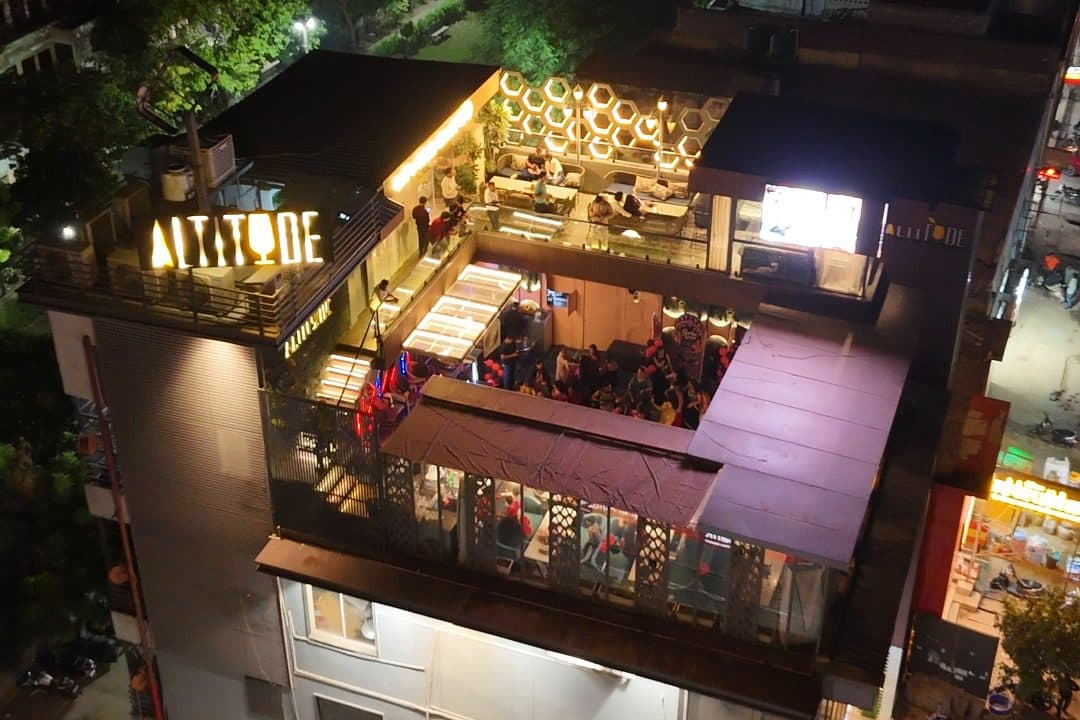The Altitude rooftop on MG Road 2 lit at night: the ALTITUDE sign on the corner of the building, the upper terrace glowing and the covered terrace below