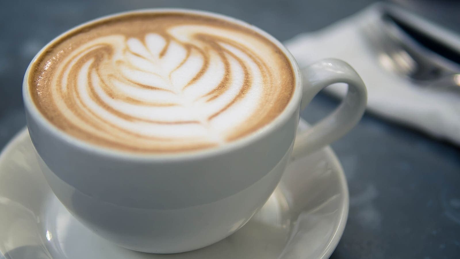 A cappuccino with a leaf drawn in its milk foam, seen from above on a wooden table