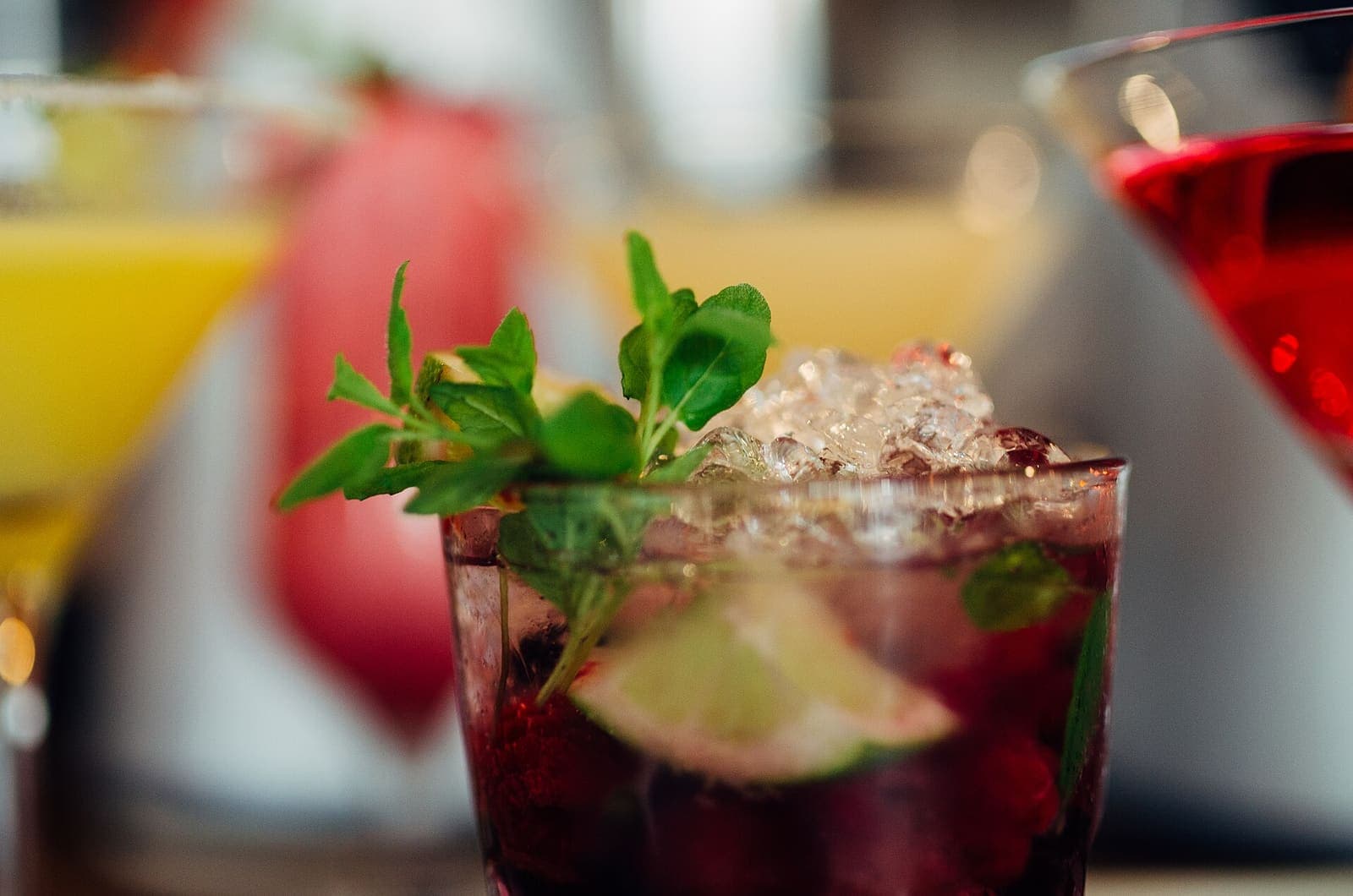 Colourful cocktails garnished with fresh fruit and herbs, lined up along a bar counter