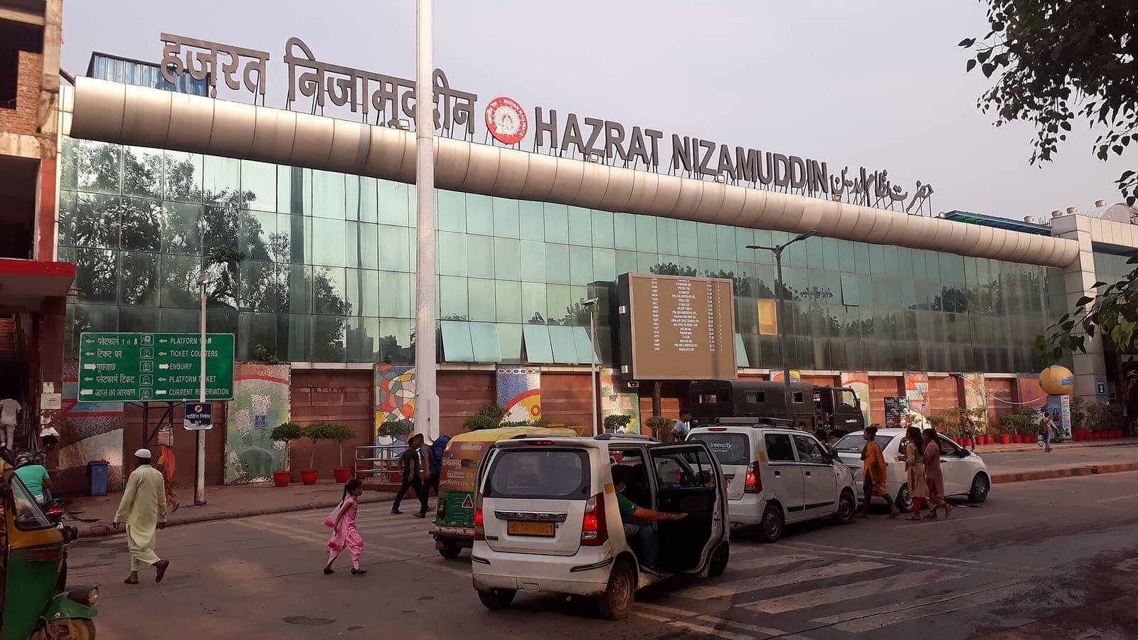The glass front of Hazrat Nizamuddin railway station in Delhi, with taxis and autos in the forecourt