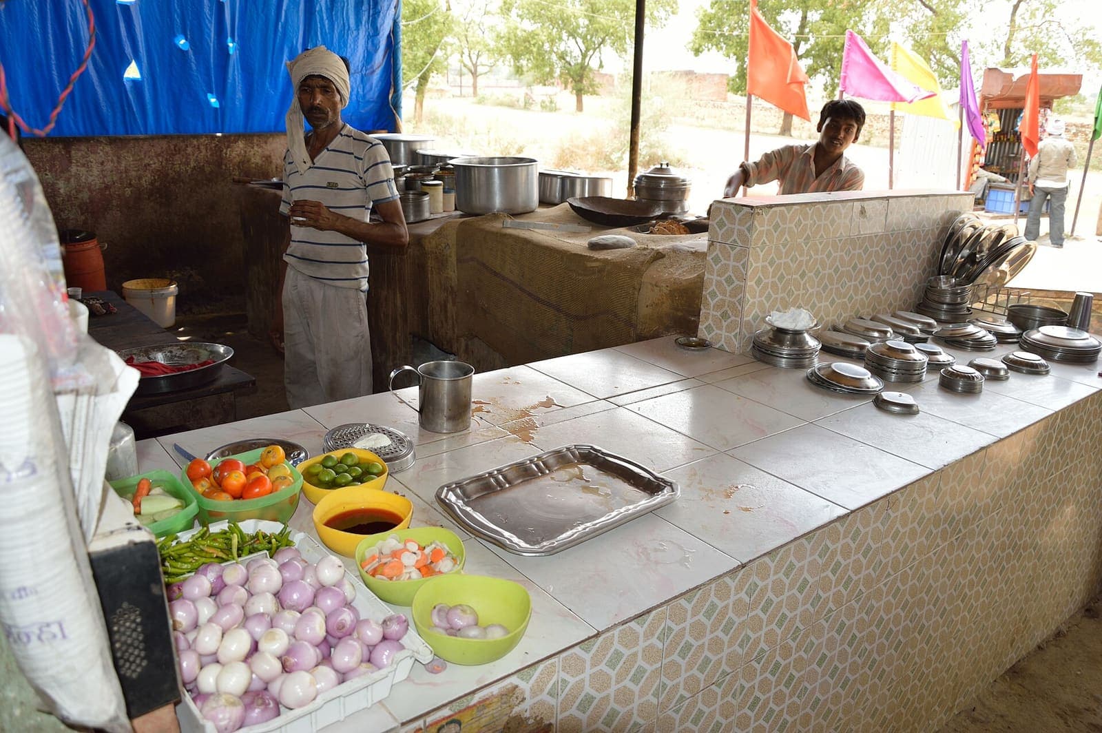 A highway dhaba’s open kitchen counter, with bowls of onions, tomatoes, green chillies and limes in front of a clay oven