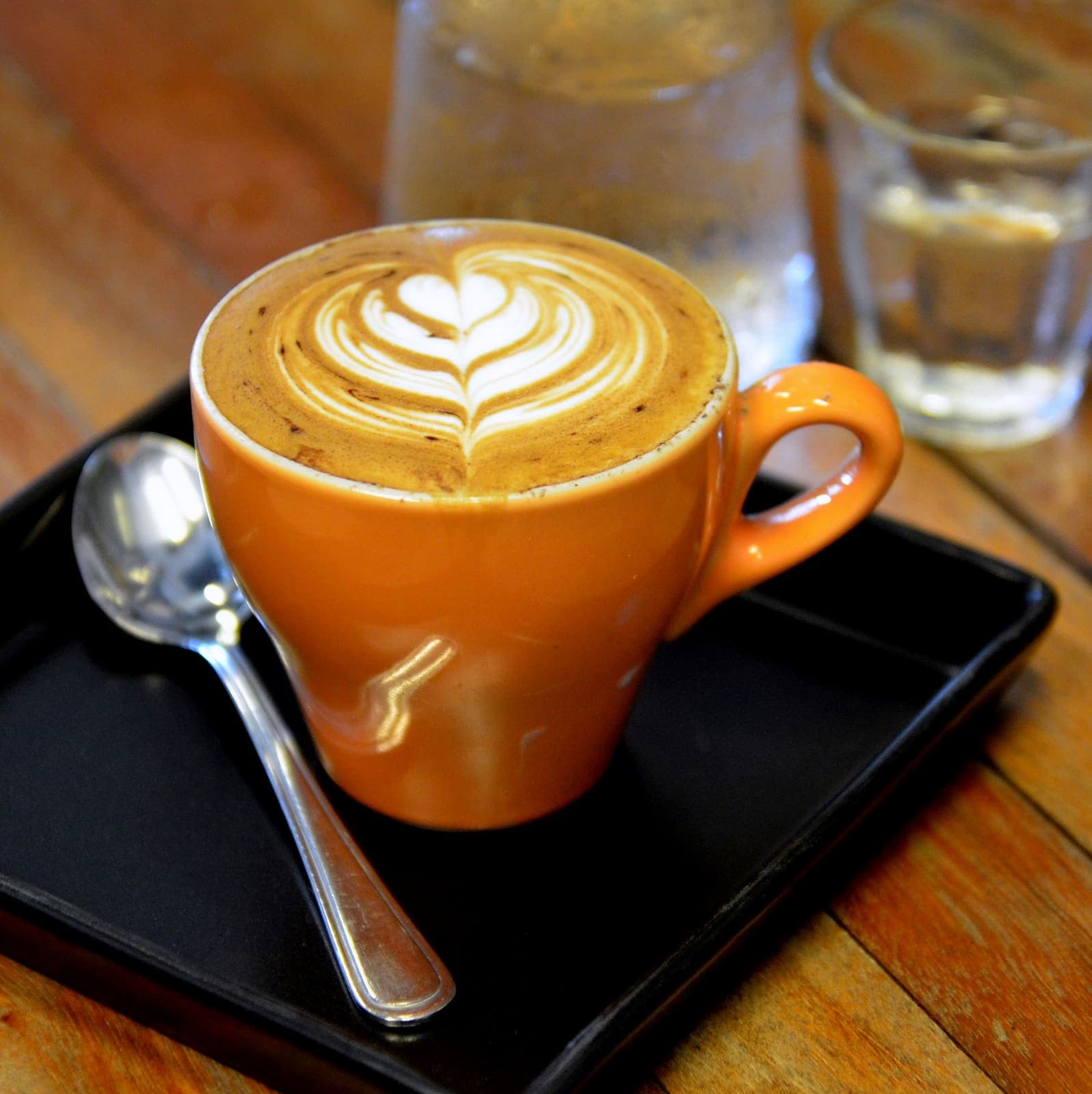 Latte art in the foam of a coffee served in an orange cup on a dark café tray
