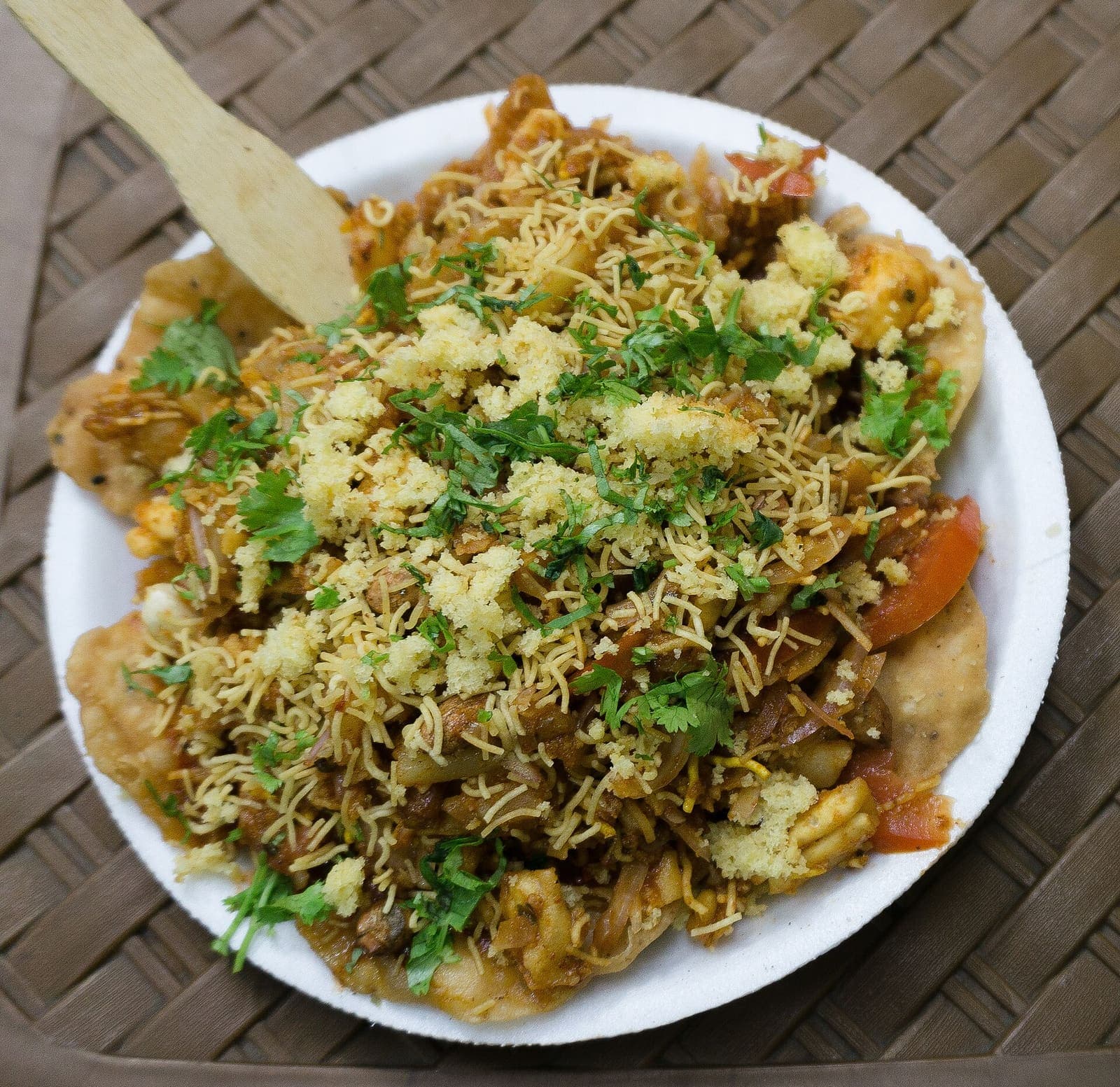 A plate of papri chaat: crisp fried wafers topped with potato, chickpeas, curd, chutneys and sev