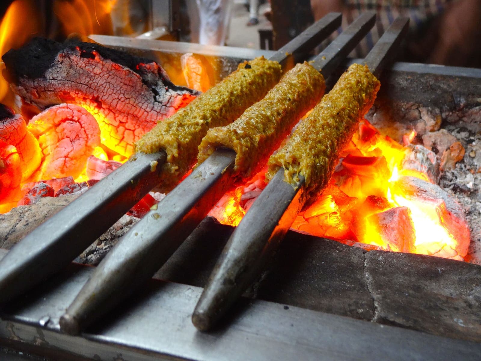 Minced-meat seekh kebabs on long metal skewers, cooking over a bed of glowing charcoal