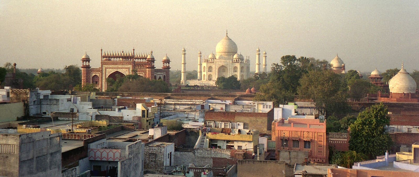Panorama over the flat rooftops of Taj Ganj, with the Taj Mahal and its sandstone gateway rising behind