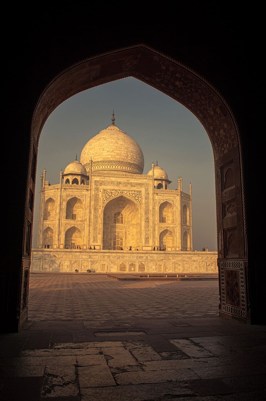 The Taj Mahal glowing gold, framed by the dark silhouette of an arched gateway