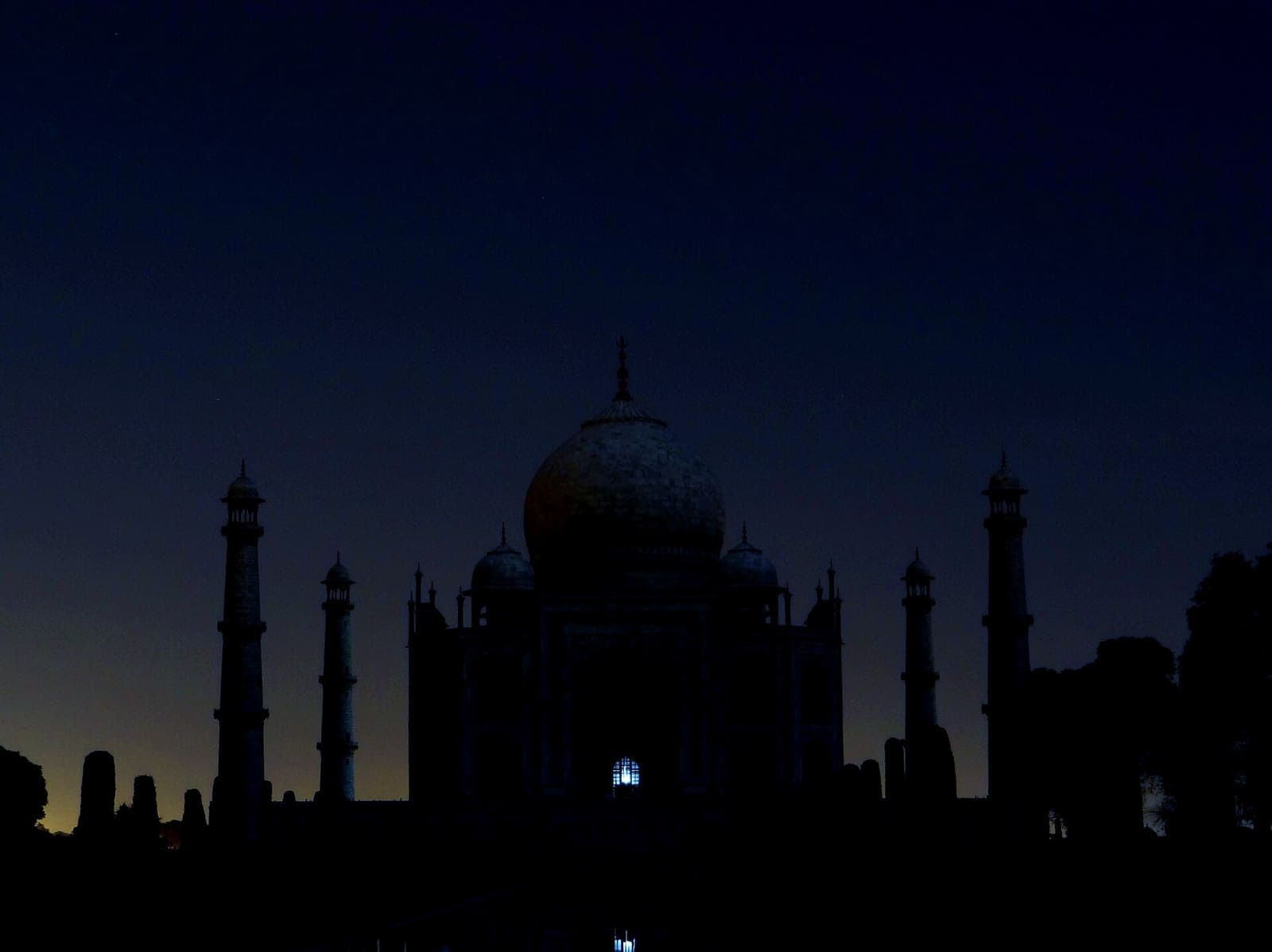 The Taj Mahal and its minarets as a dark silhouette against a deep blue night sky