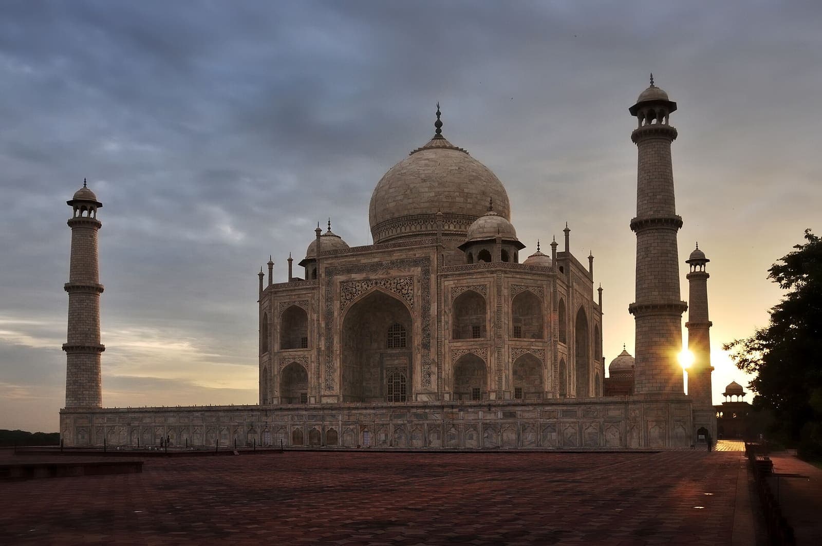 The Taj Mahal at sunrise from the forecourt, a minaret and the low sun under a dramatic sky