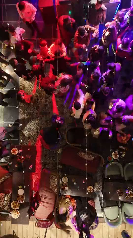 The Altitude dance floor on New Year’s Eve from straight above, packed, the drone rising until the whole roof is in frame